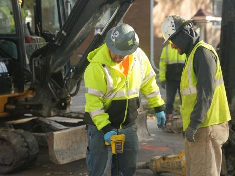 Photo of construction workers replacing a lead service pipe in the ground outside of a home.